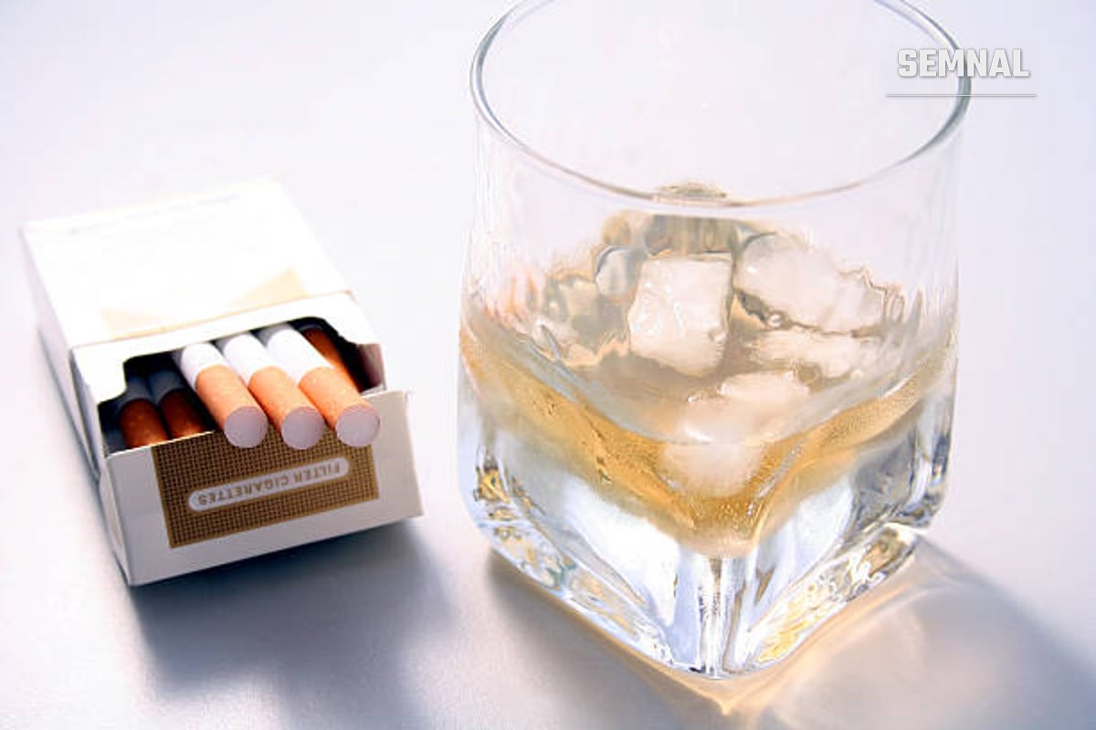 In imagine este un pahar cu alcool și cuburi de gheață, alături de un pachet de țigari desfăcut.