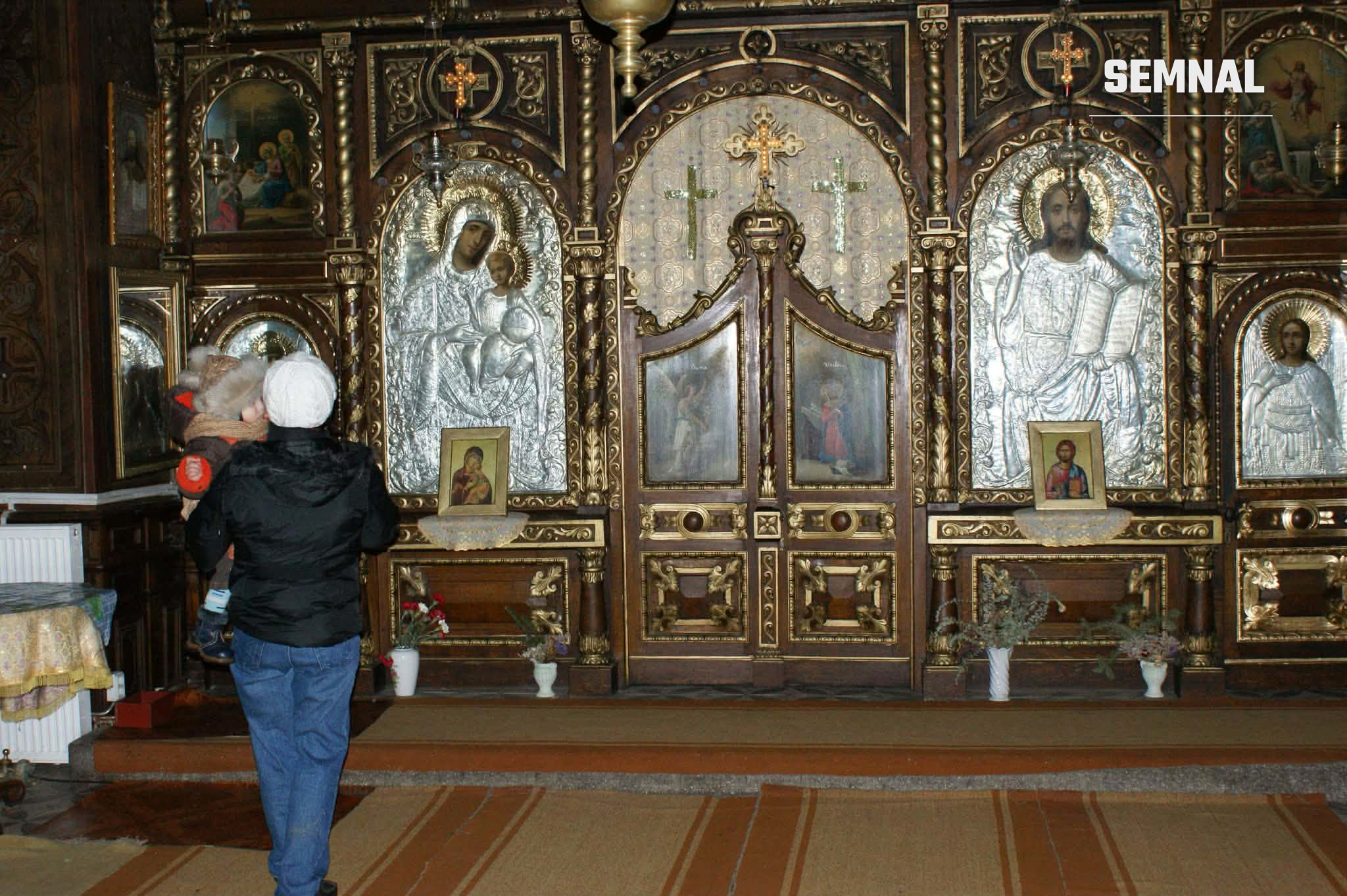 În imagine este un interior de biserică ortodoxă cu o mamă și un copil.